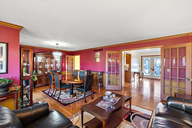 living room with a chandelier, light hardwood / wood-style floors, ornamental molding, and french doors