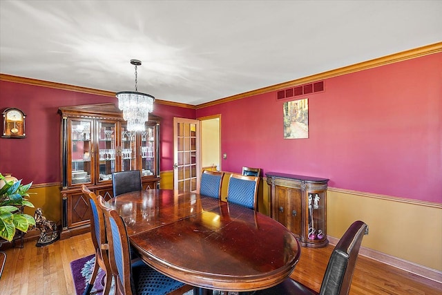 dining area featuring hardwood / wood-style flooring, ornamental molding, and a notable chandelier