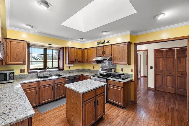 kitchen featuring appliances with stainless steel finishes, light stone counters, sink, wood-type flooring, and a center island