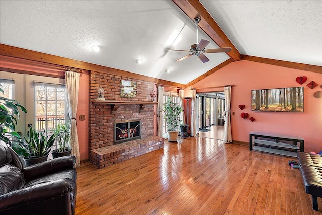 living room featuring ceiling fan, lofted ceiling with beams, a textured ceiling, and a brick fireplace