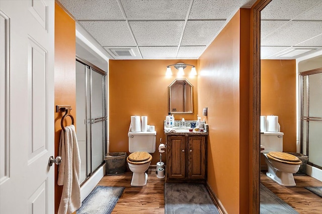 bathroom featuring vanity, a drop ceiling, a shower with door, hardwood / wood-style flooring, and toilet