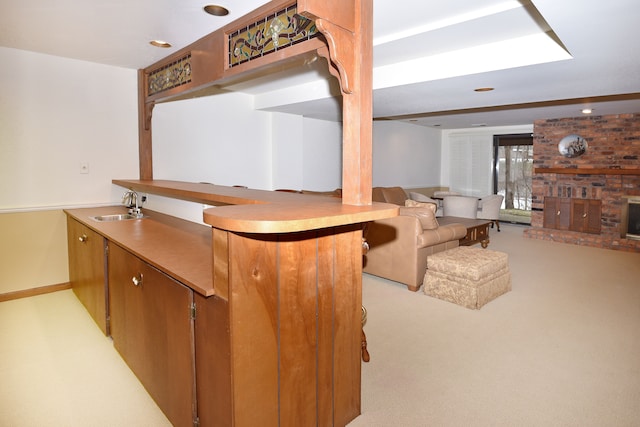 kitchen with sink, light colored carpet, kitchen peninsula, and a brick fireplace