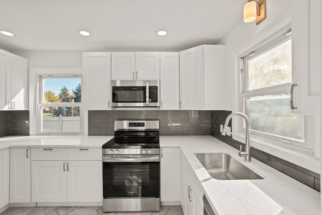 kitchen with appliances with stainless steel finishes, backsplash, light stone counters, sink, and white cabinets