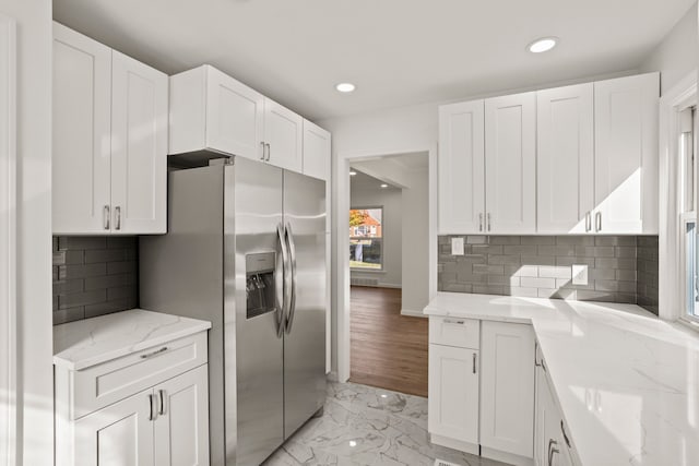 kitchen with white cabinets, stainless steel fridge with ice dispenser, decorative backsplash, and light stone countertops