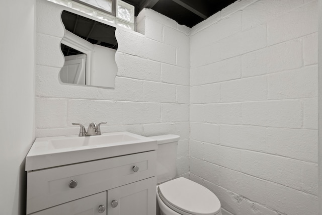 bathroom featuring vanity, toilet, and brick wall