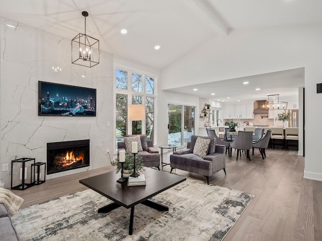 living room with high vaulted ceiling, an inviting chandelier, a high end fireplace, light hardwood / wood-style flooring, and beam ceiling