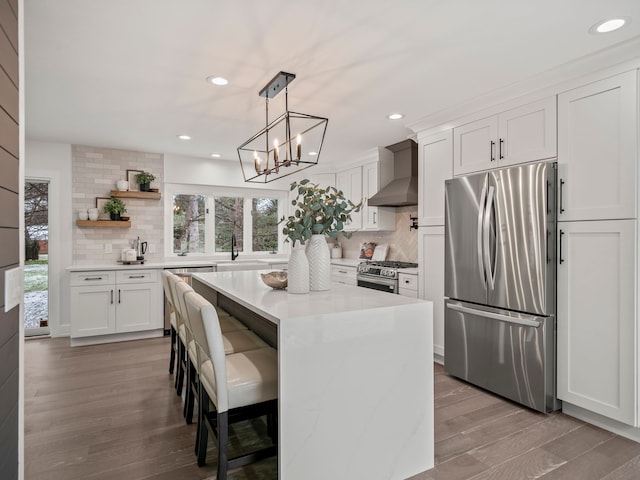 kitchen featuring backsplash, wall chimney exhaust hood, stainless steel appliances, white cabinets, and a kitchen island