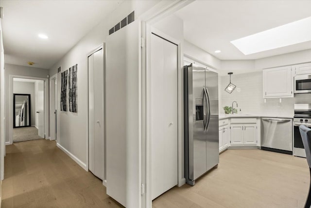 kitchen featuring white cabinets, a skylight, decorative backsplash, appliances with stainless steel finishes, and light hardwood / wood-style floors