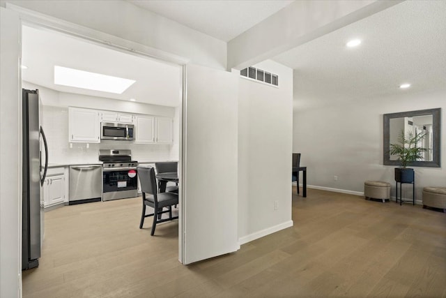 kitchen featuring decorative backsplash, appliances with stainless steel finishes, light wood-type flooring, beamed ceiling, and white cabinetry