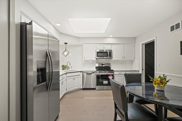 kitchen with sink, a skylight, decorative backsplash, white cabinetry, and stainless steel appliances