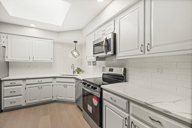 kitchen with sink, a skylight, decorative light fixtures, white cabinetry, and stainless steel appliances