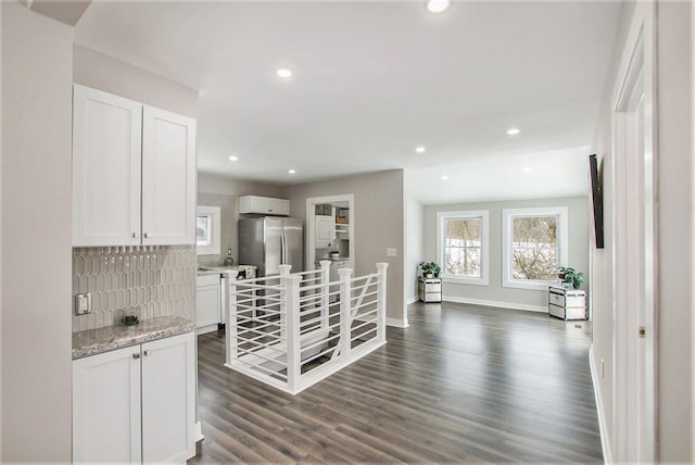 kitchen with white cabinetry, light stone counters, stainless steel refrigerator, dark hardwood / wood-style floors, and backsplash