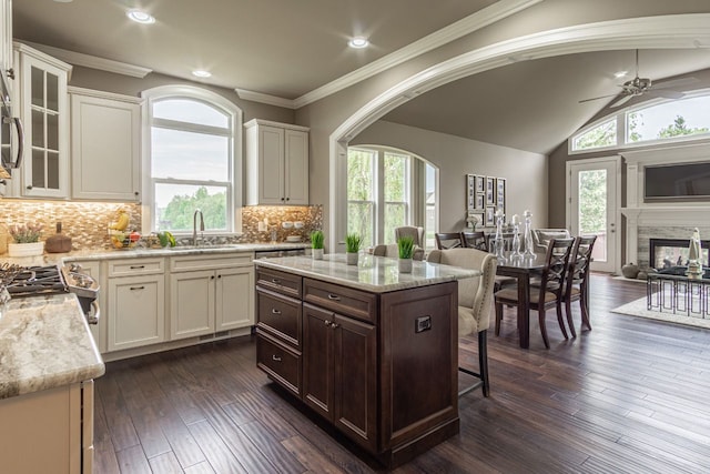 kitchen with a center island, light stone countertops, a multi sided fireplace, and sink