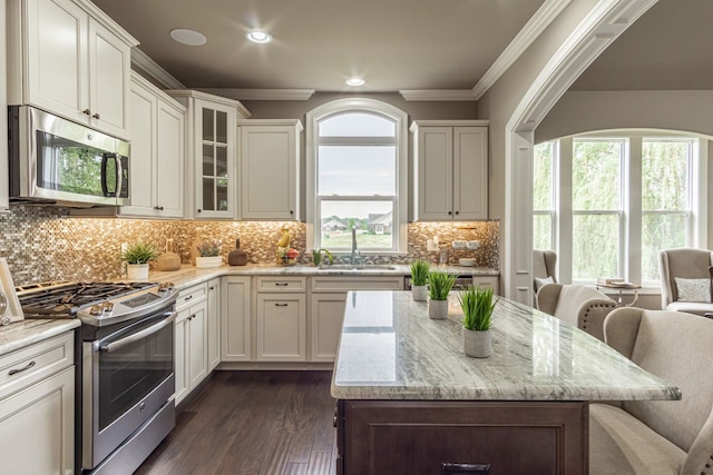 kitchen with light stone countertops, stainless steel appliances, a breakfast bar, crown molding, and white cabinetry