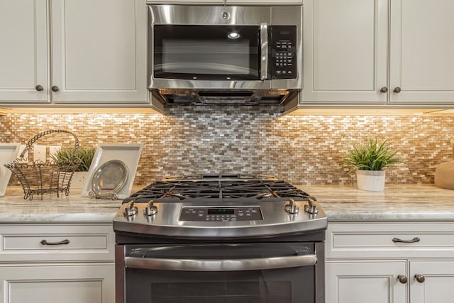 kitchen featuring light stone counters, white cabinets, appliances with stainless steel finishes, and backsplash