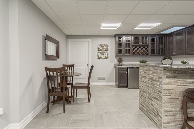 kitchen featuring dark brown cabinets, refrigerator, stainless steel dishwasher, and a drop ceiling