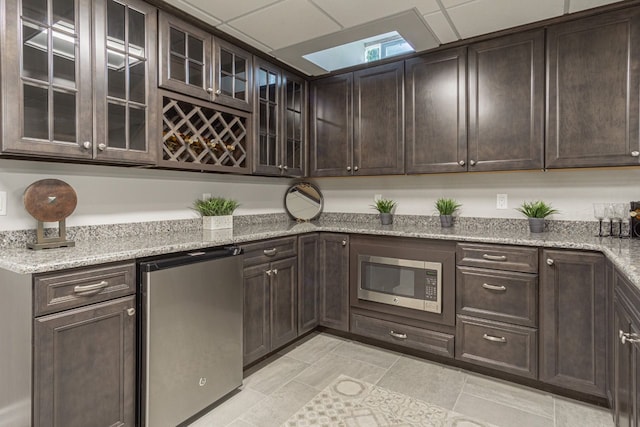 kitchen with light stone counters, refrigerator, a skylight, dark brown cabinets, and stainless steel microwave