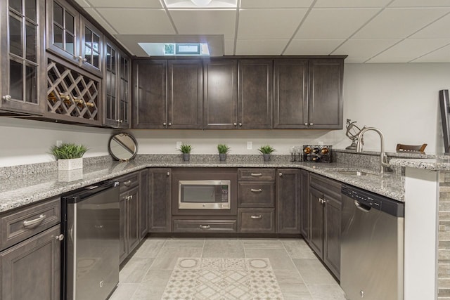 kitchen featuring appliances with stainless steel finishes, light stone counters, a drop ceiling, sink, and dark brown cabinets