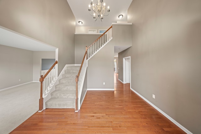 staircase with hardwood / wood-style floors, a towering ceiling, and an inviting chandelier