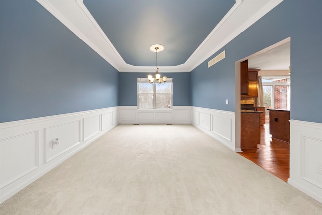 spare room featuring a notable chandelier, a raised ceiling, ornamental molding, and light carpet