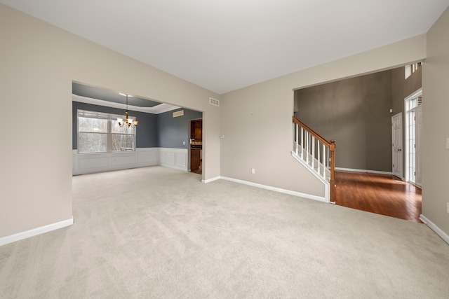 unfurnished living room featuring carpet flooring, ornamental molding, and an inviting chandelier