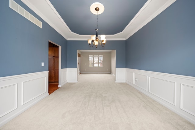 carpeted empty room with a raised ceiling, an inviting chandelier, and crown molding