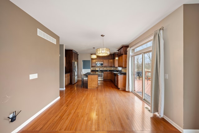 kitchen with a center island, light hardwood / wood-style floors, pendant lighting, decorative backsplash, and appliances with stainless steel finishes