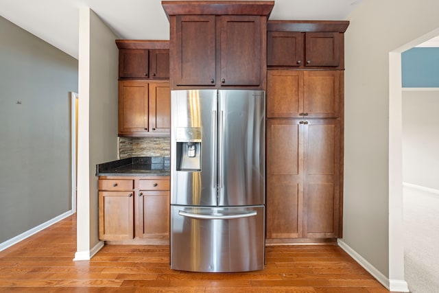 kitchen with hardwood / wood-style floors, stainless steel fridge, backsplash, and dark stone counters