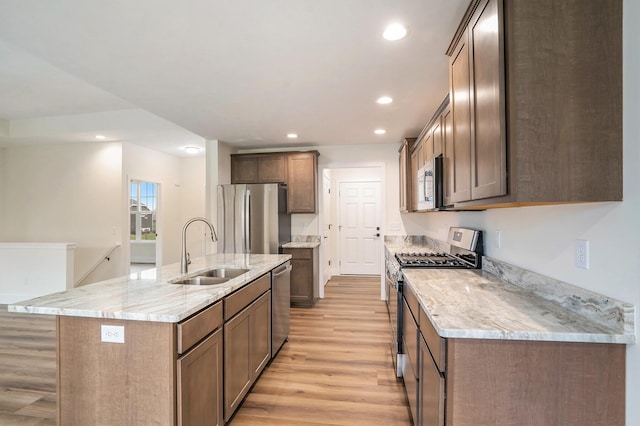 kitchen with light stone countertops, sink, light hardwood / wood-style flooring, an island with sink, and appliances with stainless steel finishes