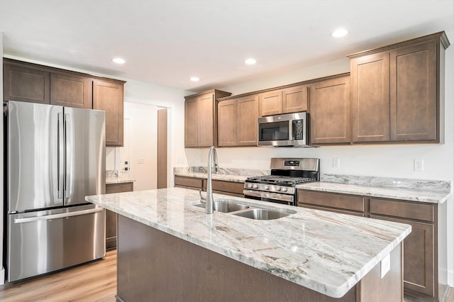 kitchen with light stone countertops, light wood-type flooring, an island with sink, and appliances with stainless steel finishes