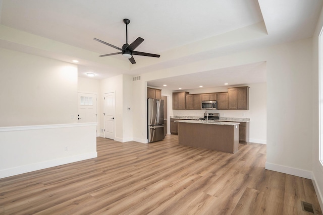 kitchen featuring ceiling fan, sink, stainless steel appliances, an island with sink, and light wood-type flooring