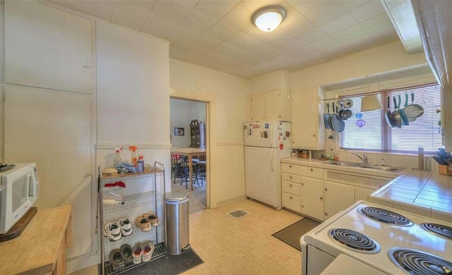 kitchen with tile counters, white cabinetry, sink, and white appliances