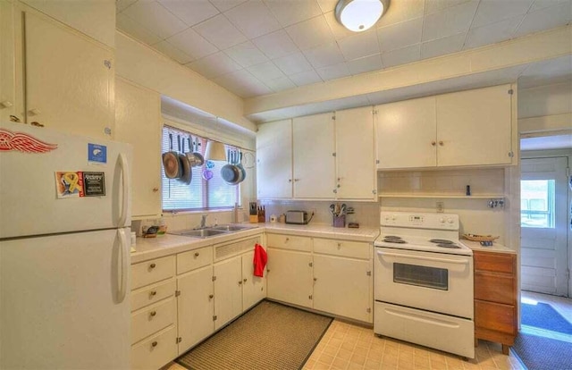 kitchen with a wealth of natural light, white cabinetry, sink, and white appliances