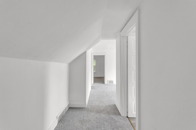 hallway with light colored carpet and lofted ceiling