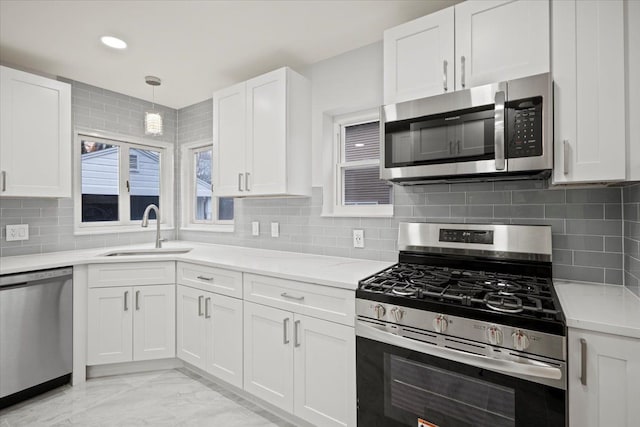 kitchen with tasteful backsplash, stainless steel appliances, sink, white cabinetry, and hanging light fixtures