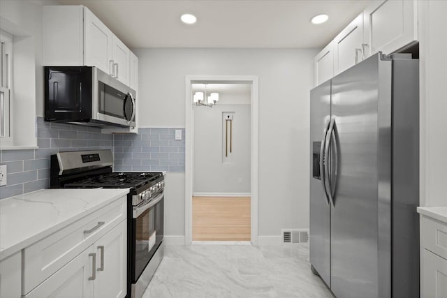 kitchen with light stone countertops, a chandelier, decorative backsplash, white cabinets, and appliances with stainless steel finishes