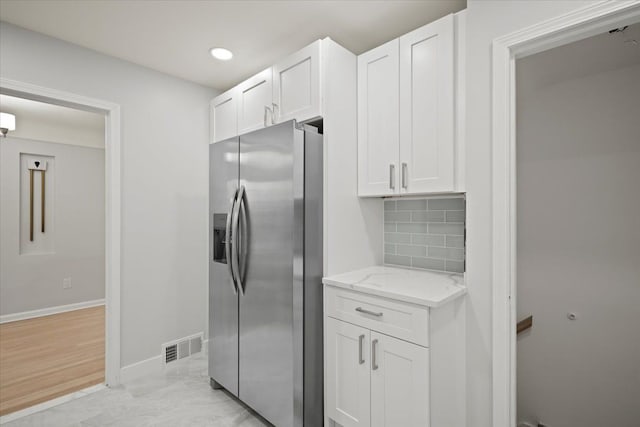 kitchen featuring white cabinets, stainless steel fridge with ice dispenser, backsplash, and light stone countertops