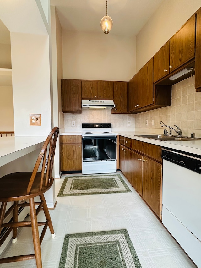 kitchen featuring decorative backsplash, white appliances, sink, pendant lighting, and a breakfast bar area