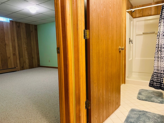 interior space featuring a paneled ceiling, wood walls, light tile patterned flooring, and a baseboard heating unit