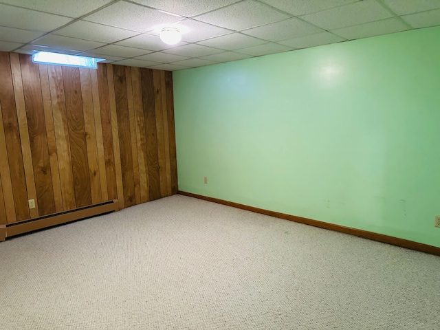 basement featuring carpet, a paneled ceiling, a baseboard heating unit, and wood walls