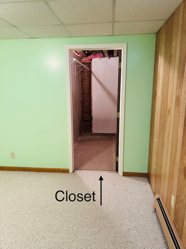 carpeted spare room with a paneled ceiling, wood walls, and a baseboard heating unit