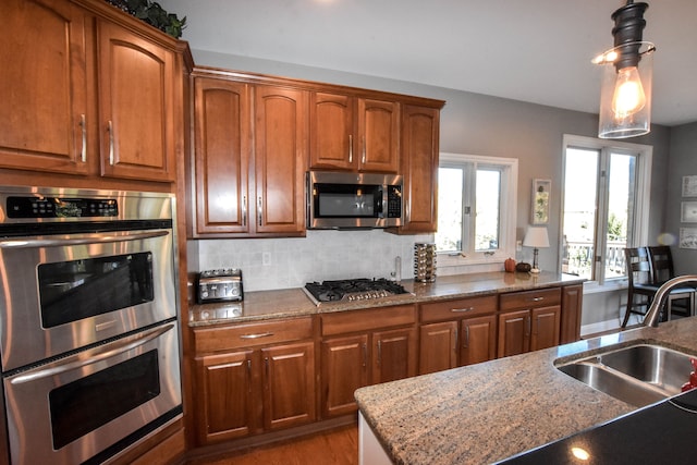 kitchen featuring light stone countertops, appliances with stainless steel finishes, backsplash, sink, and pendant lighting