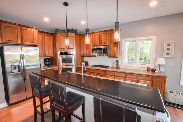 kitchen with a kitchen island with sink, hanging light fixtures, light hardwood / wood-style flooring, appliances with stainless steel finishes, and a breakfast bar area