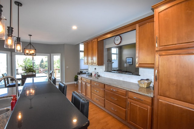 kitchen featuring sink, hanging light fixtures, dark stone counters, light hardwood / wood-style floors, and decorative backsplash