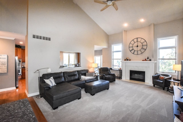 carpeted living room with a high end fireplace, high vaulted ceiling, and ceiling fan