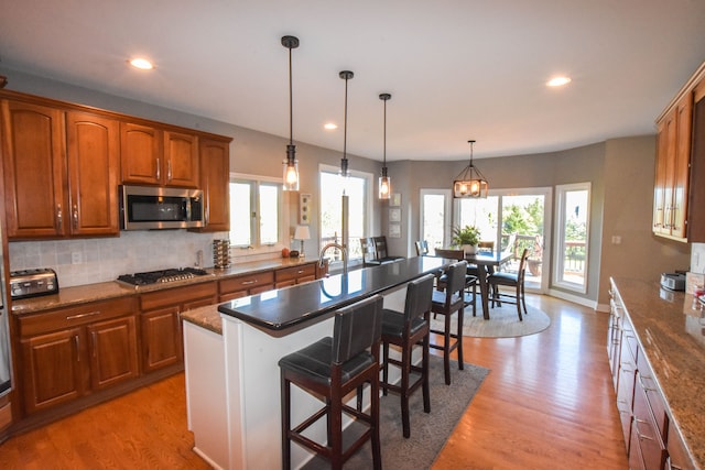 kitchen with stainless steel appliances, dark stone counters, light hardwood / wood-style floors, a kitchen bar, and a kitchen island