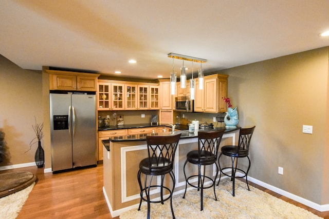 kitchen featuring a breakfast bar, hanging light fixtures, light wood-type flooring, appliances with stainless steel finishes, and kitchen peninsula