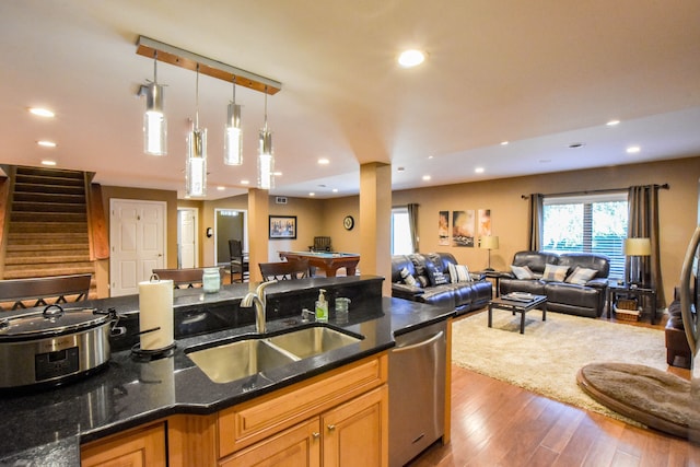 kitchen with dark stone counters, sink, stainless steel dishwasher, decorative light fixtures, and dark hardwood / wood-style flooring