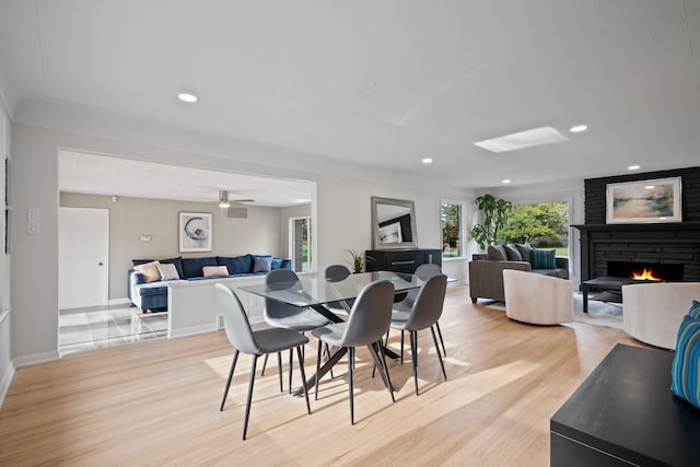 dining space with light hardwood / wood-style floors, a brick fireplace, and ceiling fan