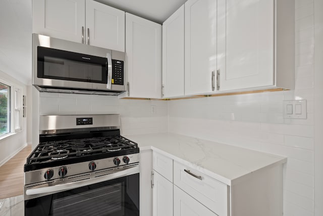 kitchen featuring hardwood / wood-style floors, backsplash, white cabinets, light stone counters, and stainless steel appliances